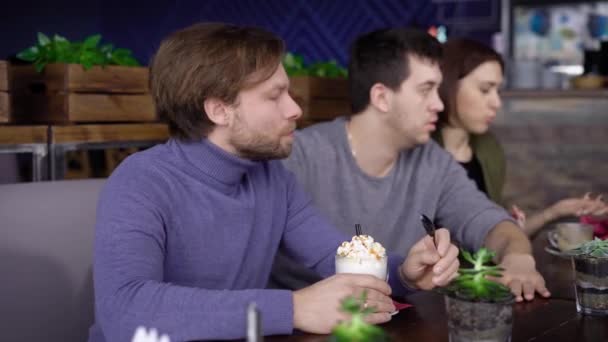 An adult middle-aged man with blond hair and a beard, dressed in a purple sweater, drinks with pleasure frappuchino coffee with whipped cream — Stock Video
