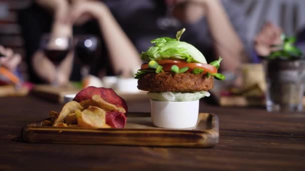 A healthy vegetable hamburger made from carrot chops, with tomato slices, lettuce leaves and soybean seedlings on onion cushion served on a wooden tray with vegetable chips and sauce — Stock Video