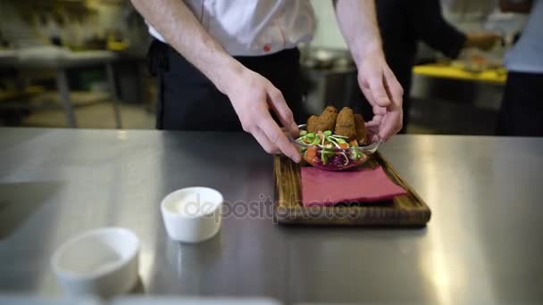 Primer plano de la mano de los chefs, que pone la salsa en una bandeja de madera, donde ya hay una ensalada y falafel vegetal, entonces este plato se llevará a la habitación de invitados — Vídeos de Stock