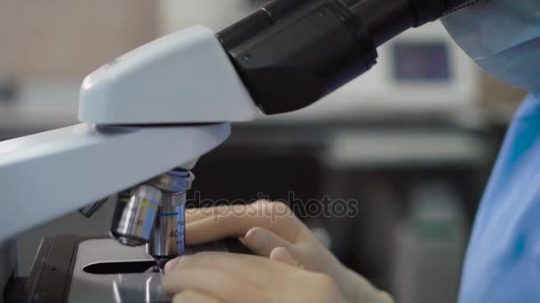 Plan de culture d'un travailleur de laboratoire au microscope. Plan sans visage de la femelle spécialiste en uniforme en utilisant un microscope . — Video