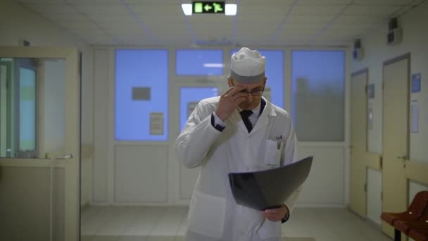 Зрілий чоловік лікар з рентгенограмою. Чоловік лікар в уніформі ходить в лікарні з радіограмою і досліджує її . — стокове відео
