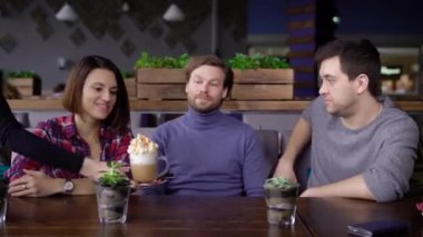 Mutlu genç arkadaşlarla kafede oturan ve tatlı lezzetli tatlı krem şanti ile olan adam. Kahvaltı ve onun arkadaşları arkadaşlarının süt köpüklü cappuccino kahve içme ve gülümseyen öğrenci.