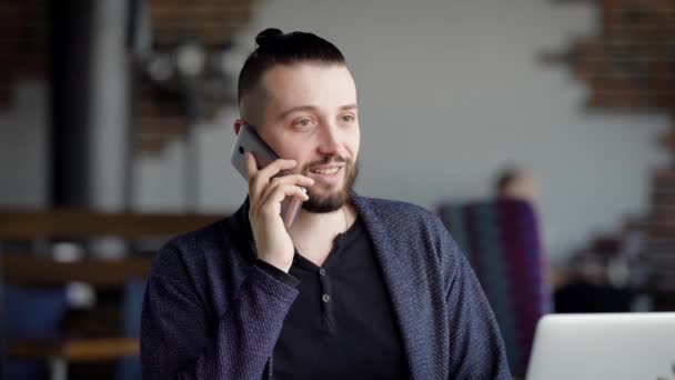 Genç çekici hippi bir kafe, modern iç. Bir adam bir arkadaş veya iş arkadaşı ile telefonda konuşuyor. Adam sonu iyi bir ruh hali. — Stok video