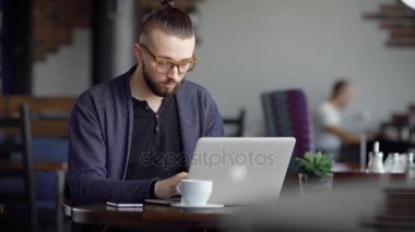 Genç çekici hippi bir kafe, modern iç. Adam onun şık dizüstü bilgisayarda çalışıyor. Bir tasarımcı ya da bir yazar bir kafede bir proje yapar.