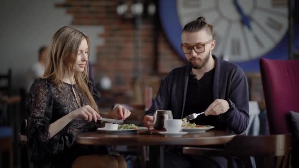 A couple, a man and a woman in a modern restaurant, have lunch or dinner. A man and a woman enjoy food and have a social conversation. In love, they laugh because they have a date. — Stock Video