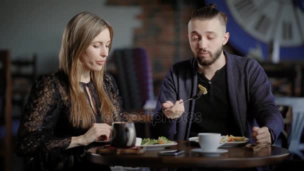 Um casal, um homem e uma mulher num restaurante moderno, almoçam ou jantam. Um homem e uma mulher gostam de comida e têm uma conversa social. Marido e esposa são felizes no casamento, eles têm um dia de folga — Vídeo de Stock