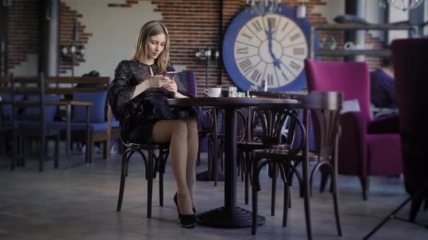 Joven linda mujer usando el teléfono, sentado en un café con un teléfono inteligente, contestando mensajes de texto. Hermosa mujer de negocios en un restaurante durante una pausa para el almuerzo, mensajes de navegación en línea . — Vídeo de stock