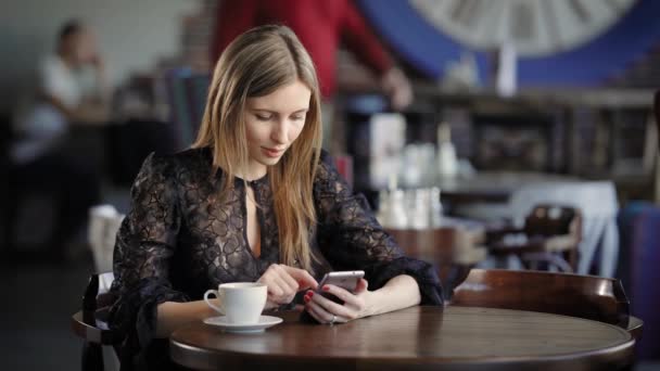 Roztomilý dívka pomocí telefonu, sedí v kavárně držení smartphone, odpovídání texty. Krásný obchodní žena v restauraci během přestávky na oběd, procházení zpráv online. — Stock video