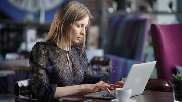 Όμορφη γυναίκα σε μια καφετέρια που λειτουργεί με έναν φορητό υπολογιστή. Κυρία σοβαρή επιχείρηση, εκτελεί μια παραγγελία μέσω Διαδικτύου κατά τη διάρκεια του μεσημεριανού διαλείμματος. Σύγχρονη ασύρματη τεχνολογία — Αρχείο Βίντεο