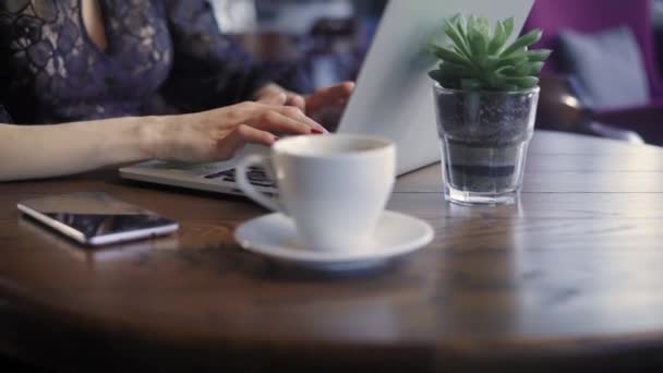 Hermosa mujer en un café trabajando con un portátil. Una chica alegre y feliz, impresiones en el teclado de las computadoras portátiles, recibió buenas noticias, y las comparte a través de las redes sociales . — Vídeos de Stock