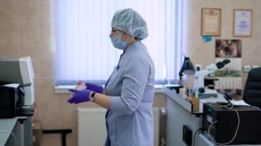 Mavi önlük, maske, kap ve ekipman için kan örnekleri ile test tüpleri aktarma ve tıbbi laboratuvar muayene hazırlanıyor lateks eldiven profesyonel kadın tıbbi bilim adamı.