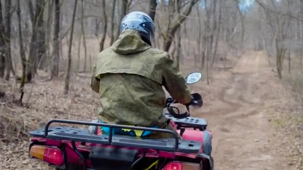 En vuxen man i kamouflage kläder och en skyddande hjälm på huvudet Rider runt i skogen på en förfallande fyrhjuling — Stockvideo