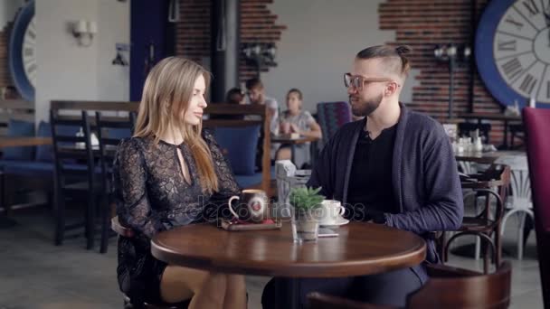 Пара влюбленных пьет кофе в ресторане, они сидят за деревянным столом и болтают с улыбкой друг с другом немного флиртуют — стоковое видео