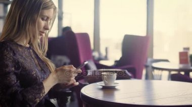 Çekici bir kadın, bir kafede kahve içer, o sosyal ağlar Internet üzerinden bir smartphone üzerinde arkadaşları ile iletişim kurar