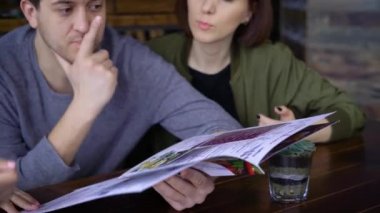 Bir önlük giyen bir garson kız üç arkadaş bir restoranda oturur ve yemekleri menüsünden siyah saçlı bir sipariş kabul eder.