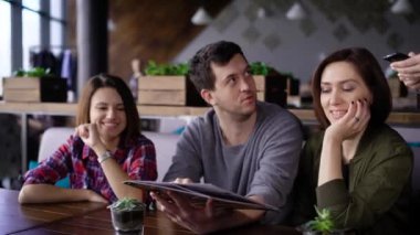 Bir önlük giyen bir garson kız üç arkadaş bir restoranda oturur ve yemekleri menüsünden siyah saçlı bir sipariş kabul eder.