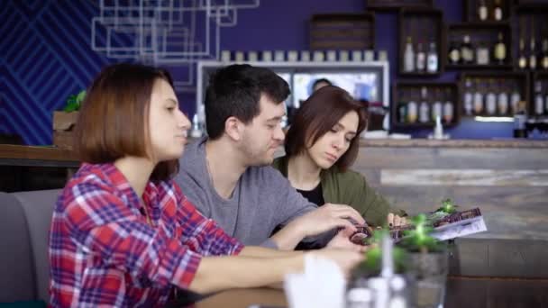 Tre vänner sitter i baren och titta igenom menyn — Stockvideo