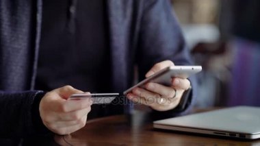 Erkek el smartphone plastik kart numarası yazarak kapatın. Genç adam modern cihaz yardımı ile fatura ödeme kafede. Masada oturan ve Ürünler internet alışveriş müşteri.