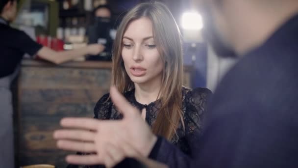 Närbild av vacker kvinna med långt ljust hår gratis umgås i restaurangen. Bedårande dam med naturlig make-up i svart spetsklänning talar med manliga händer gestikulerade i förgrunden. — Stockvideo
