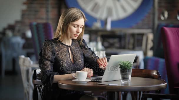 Hermosa mujer en vestido sexy negro sentado en la mesa en el restaurante utilizando el ordenador portátil moderno. Famoso blogger de belleza trabajando en una oficina móvil en una cafetería charlando con seguidores en un dispositivo digital . — Vídeos de Stock