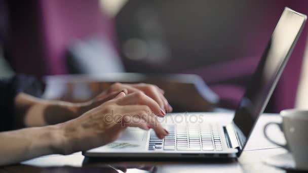 Feche de mãos elegantes femininas com pregos vermelhos que digitam o texto no teclado do computador portátil. Jovem empresária está sentada à mesa com dispositivo digital e trabalhando pressionando chaves . — Vídeo de Stock