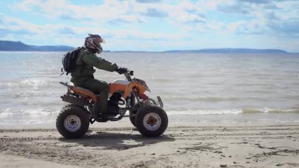 Cross quad, go by the beach. A man on an ATV, performs tricks, and drives in an extreme manner. The athlete wears a motorcycle in a helmet. Extreme vacation on the bank of the river — Stock Video