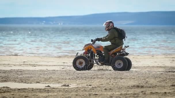 Cross Quad, ve por la playa. Un hombre en un ATV, realiza trucos, y conduce de una manera extrema. El atleta lleva una motocicleta en un casco. Vacaciones extremas en la orilla del río — Vídeos de Stock