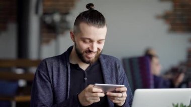 Telefon ile genç gülümseyen adam. Dizüstü bilgisayar ile kafede oturan ve telefon kullanarak genç yenilikçi.