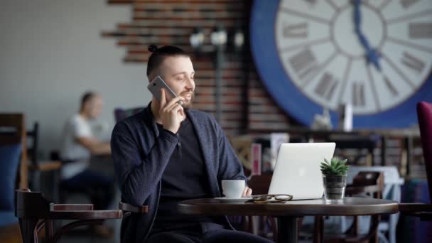 Jovem homem bem sucedido falando telefone. Jovem elegante masculino falando telefone enquanto sentado no café com laptop . — Vídeo de Stock