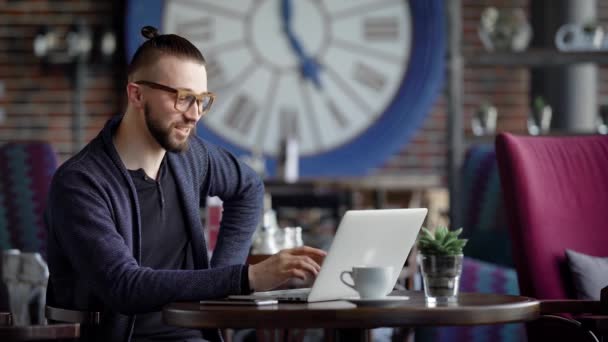 Giovane maschio usando il computer portatile. Giovane maschio sorridente seduto a tavola nel caffè e utilizzando il computer portatile . — Video Stock