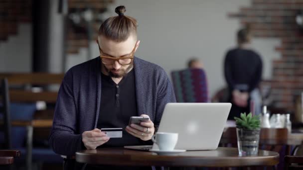 Jeune homme faisant des achats sur Internet. Jeune homme dans des lunettes assis avec ordinateur portable au café et faire l'achat Internet . — Video