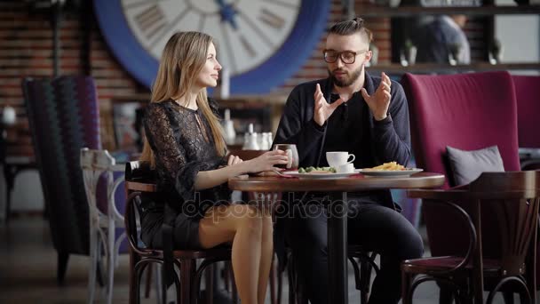 Mladý pár těší čas v kavárně. Mladé stylové pár sedí u stolu v kavárně a mluví. — Stock video
