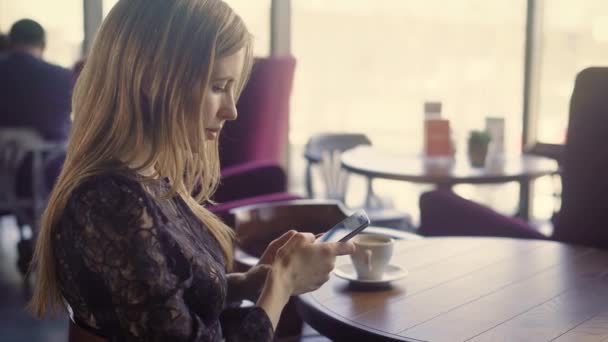 Giovane bella femmina usando il telefono. Giovane femmina attraente in abito elegante seduto a tavola con caffè e utilizzando smartphone . — Video Stock