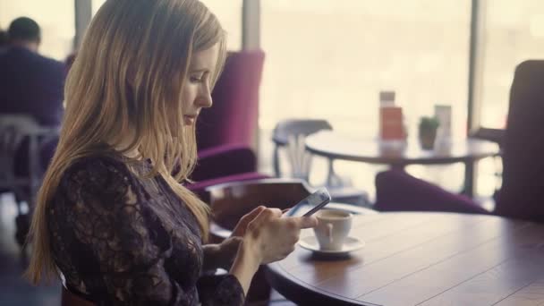 Joven linda mujer usando el teléfono. Joven mujer atractiva en vestido elegante sentado en la mesa con café y el uso de teléfono inteligente . — Vídeos de Stock