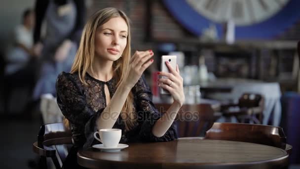 Leende flicka tar selfie. Ung leende kvinna klumpiga klänning sitter vid bord i café och tar selfie. — Stockvideo