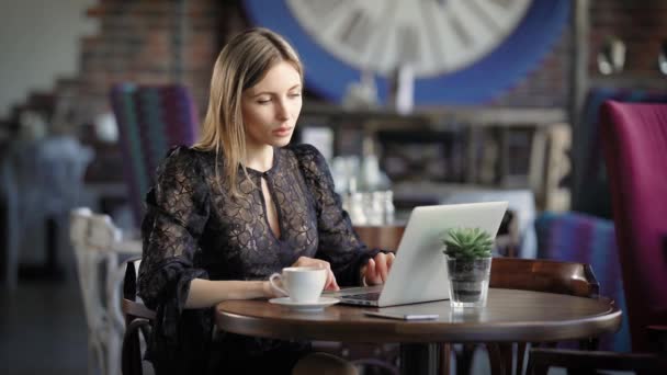 Hermosa chica con portátil. Joven mujer atractiva sentado en la cafetería y el uso de ordenador portátil . — Vídeo de stock