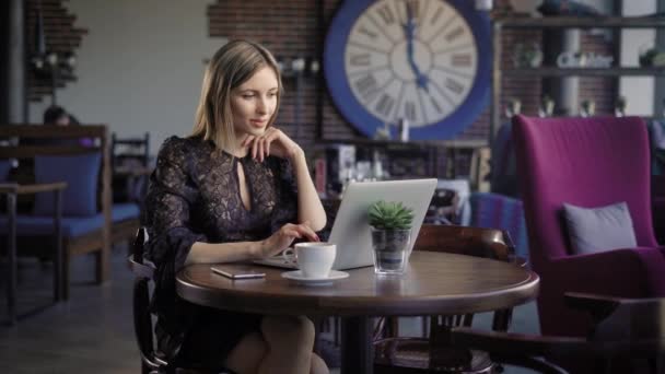 Mooie jonge meisje met laptop werken. Jonge vrouw draagt elegante jurk met behulp van laptop zittend in café. — Stockvideo