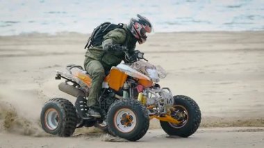 Koruyucu ekipman ve onun Atv denizin içinde belgili tanımlık geçmiş ile sahilde üzerinde sürüklenen kask adamın kapatın. Onun quad bisiklet sürme ve kıyıda toz etrafında hareket aşırı atlet.