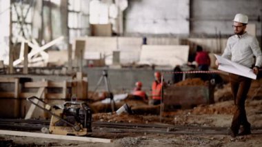 Yetişkin bir mimar inşaat yer alarak, bir kişi karşılaştırır nerede bir şantiye planı ve çizimler nesnesiyle inceliyor.