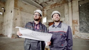 Bu yeniden oluşturmak için fabrika binasında inşaatçılar başlarını ve özel kıyafetler koruyucu bir kask bakmak iki adam,