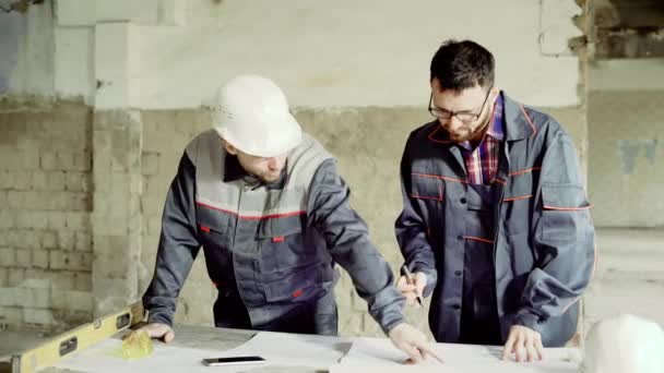 Inżynier i majster w kask ochronny robić notatki w rysunkach budowlanych, mężczyźni są w fabryce, który zostanie poddany recon budowlany — Wideo stockowe