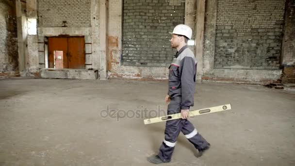 Un hombre constructor con un nivel de espíritu en su mano que mide la correspondencia de verticales u horizontales del plano se acerca a un ingeniero en una obra de construcción — Vídeos de Stock