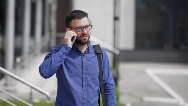 An office worker, perhaps a manager, is talking on his mobile phone on the street near his work during the day, he is in dialogue with his superiors — Stock Video