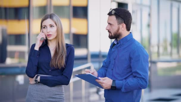 La señora de los negocios y su asistente están hablando en un teléfono móvil con un gran inversor en la calle, el hombre toma notas en documentos — Vídeo de stock