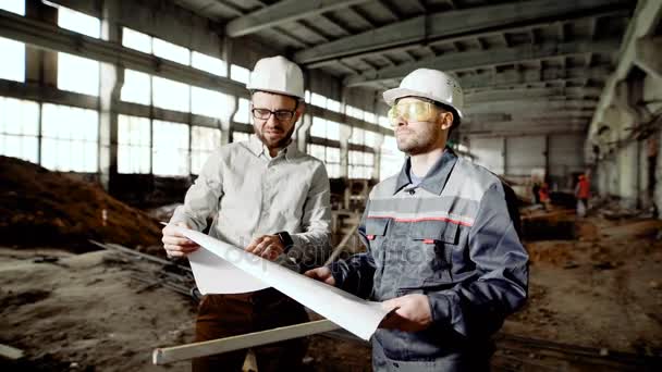 Capataz e ingeniero jefe en el sitio de construcción de la fábrica. El ingeniero comprueba el dibujo y discute otros planes con el empleado . — Vídeo de stock