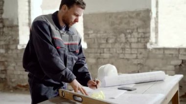 Bina nesne. Asıl çizim ile masada. Adam görünüyor ve inşaat projesi ana planı düzeltir.