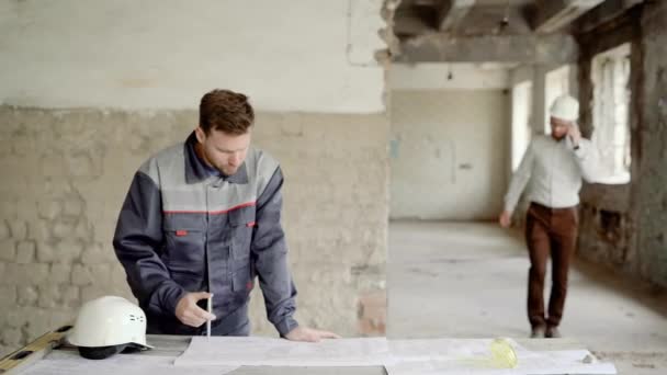 Bouw. Een zakenman op een gebouw construction site praten over de telefoon benaderingen van de tabel met een tekening. — Stockvideo