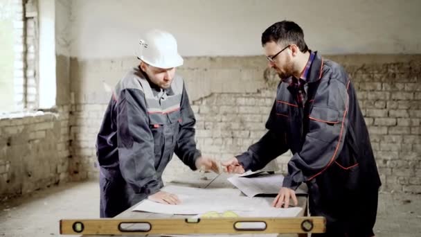 Ένας εργοδηγός και ένας υπάλληλος στο κτίριο του εργοταξίου. Ο δάσκαλος ελέγχει το σχέδιο και ολοκληρώνει το σχέδιο. — Αρχείο Βίντεο