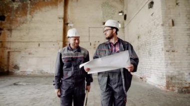 İşçi ve foreman atölye inşaat sahasında. Oluşturucu özel üniformalı ve onun baş gösterir bir kask ile giyinmiş Ustabaşıyla yapılan çalışmaları.