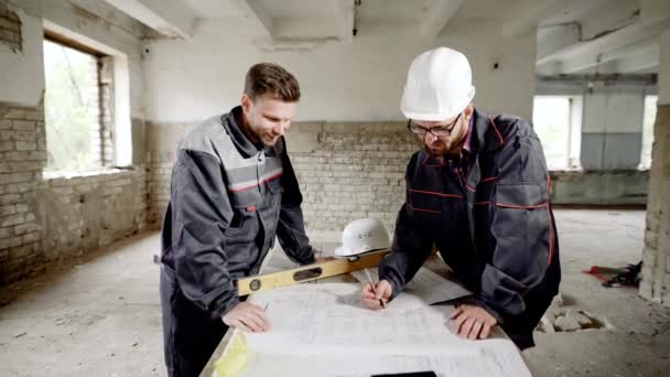 Costruire oggetti. Maestro e operaio a tavola con un disegno. Il caposquadra guarda attraverso e corregge il piano principale del progetto di costruzione . — Video Stock